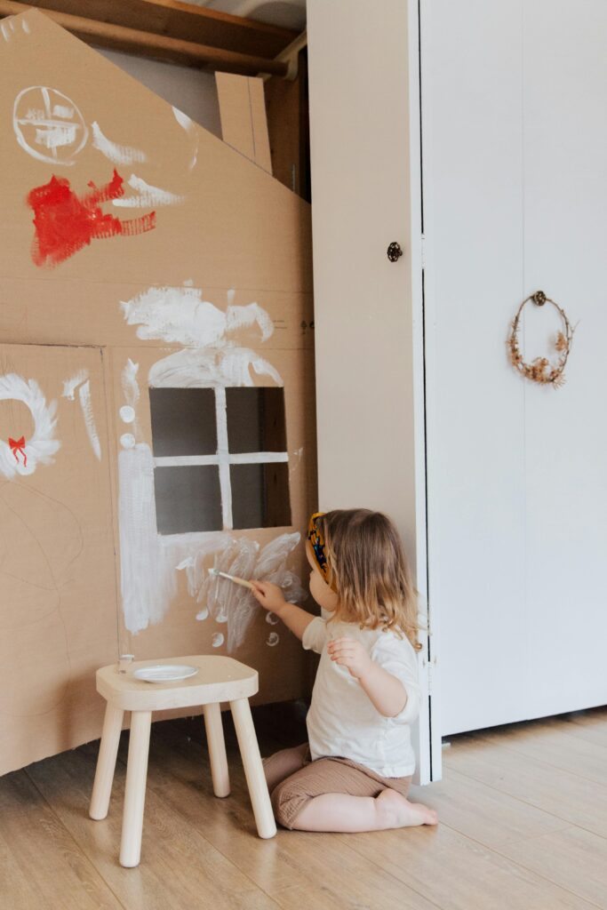 Little girl painting a cardboard house in a cozy indoor setting, expressing creativity.