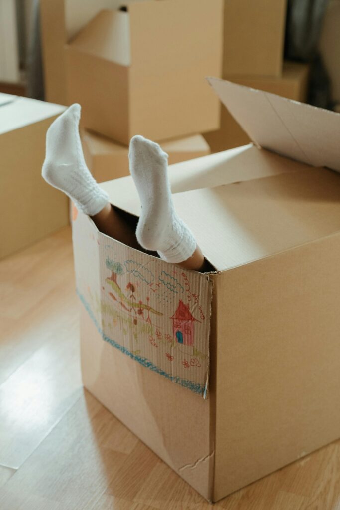 A child's feet in socks sticking out of a cardboard box inside a home, symbolizing fun and imagination during moving.