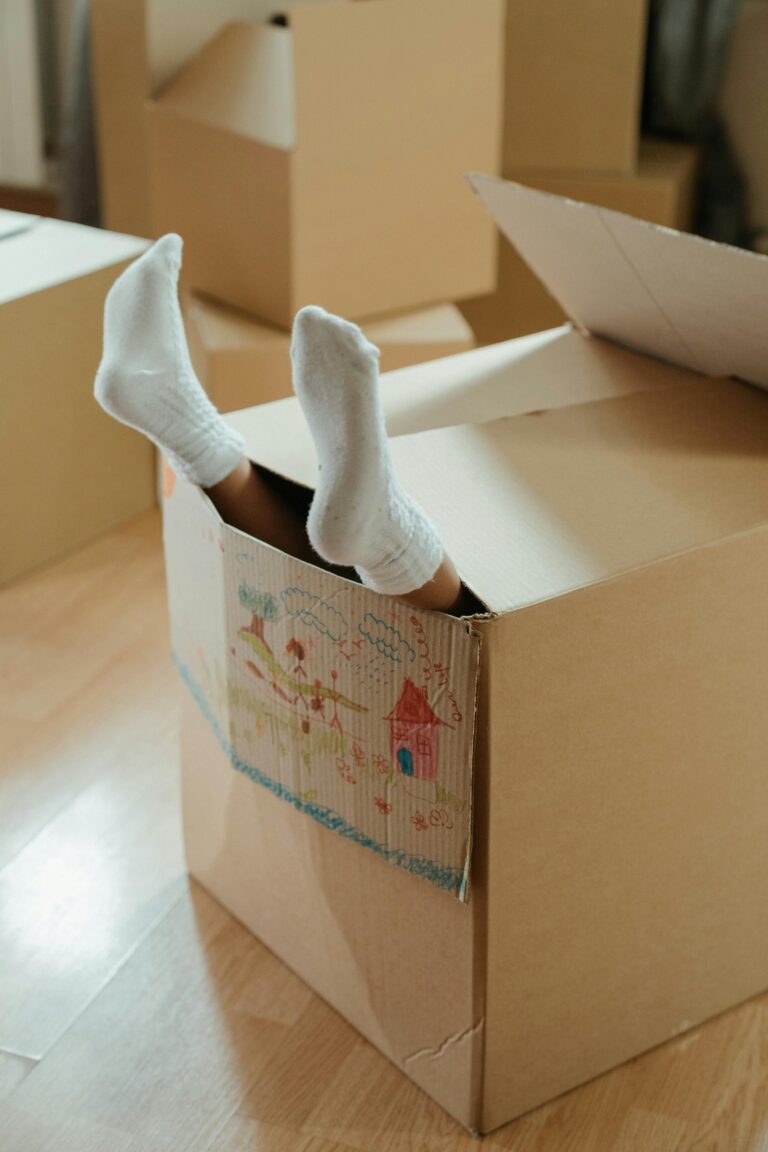 A child's feet in socks sticking out of a cardboard box inside a home, symbolizing fun and imagination during moving.
