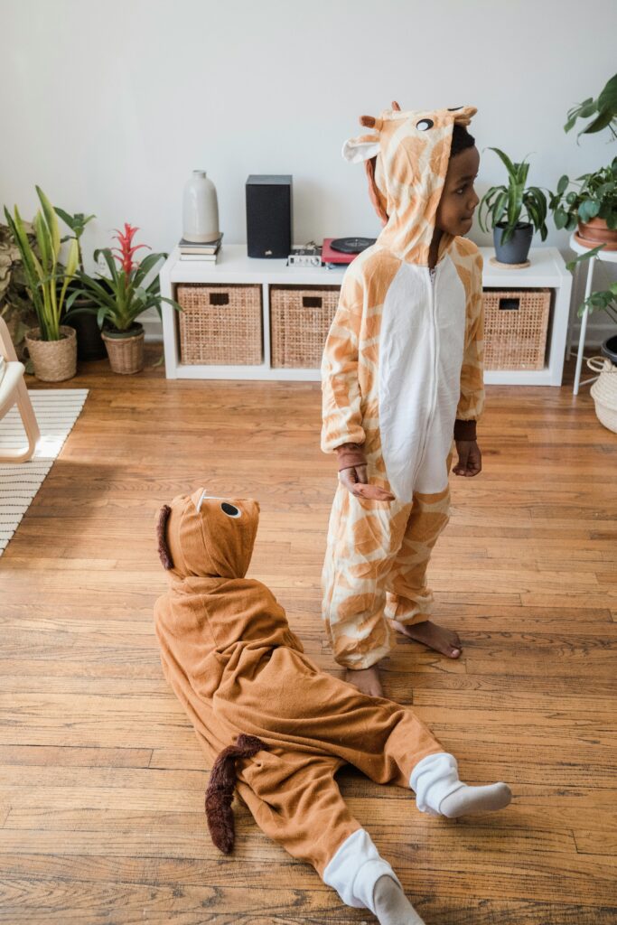 Two children wearing cute animal onesies play on a wooden floor in a cozy room.